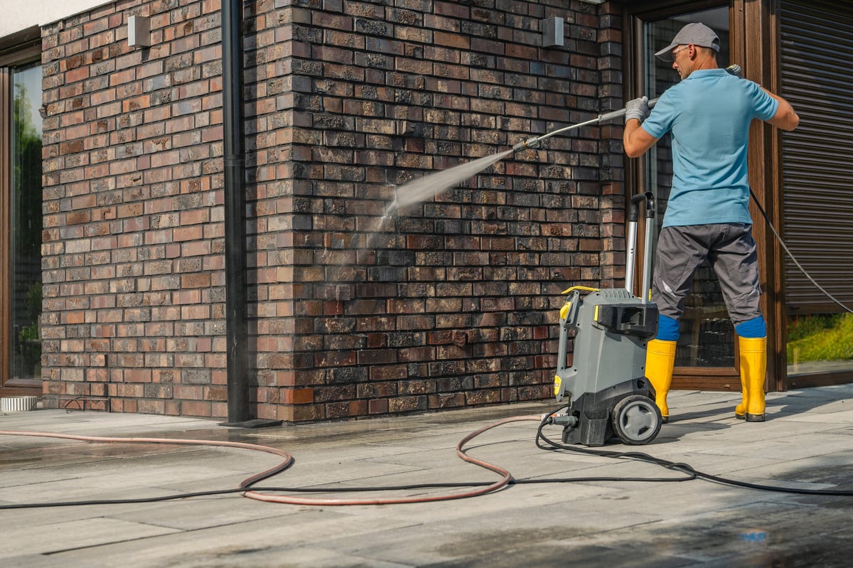 Worker pressure washing a brick wall and sidewalk