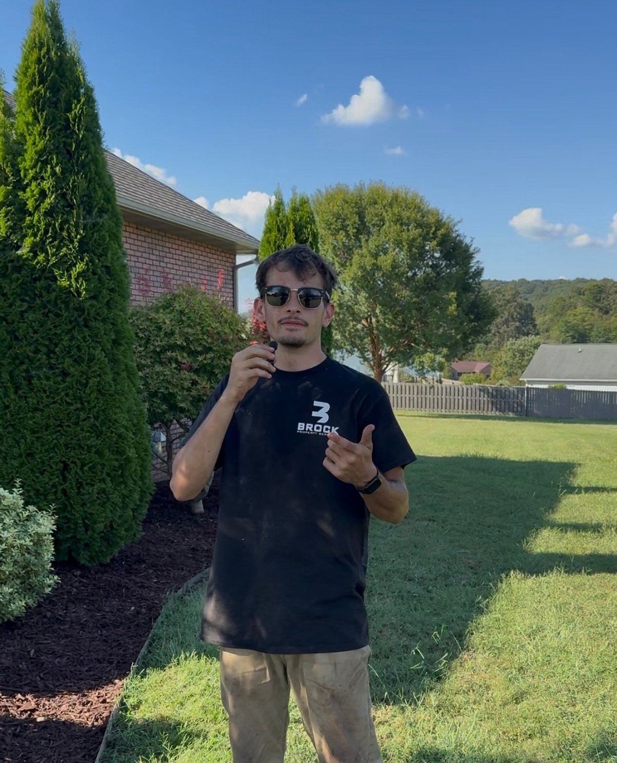 Brock Property Services team member standing in a maintained backyard with a brick home and green landscaping behind him