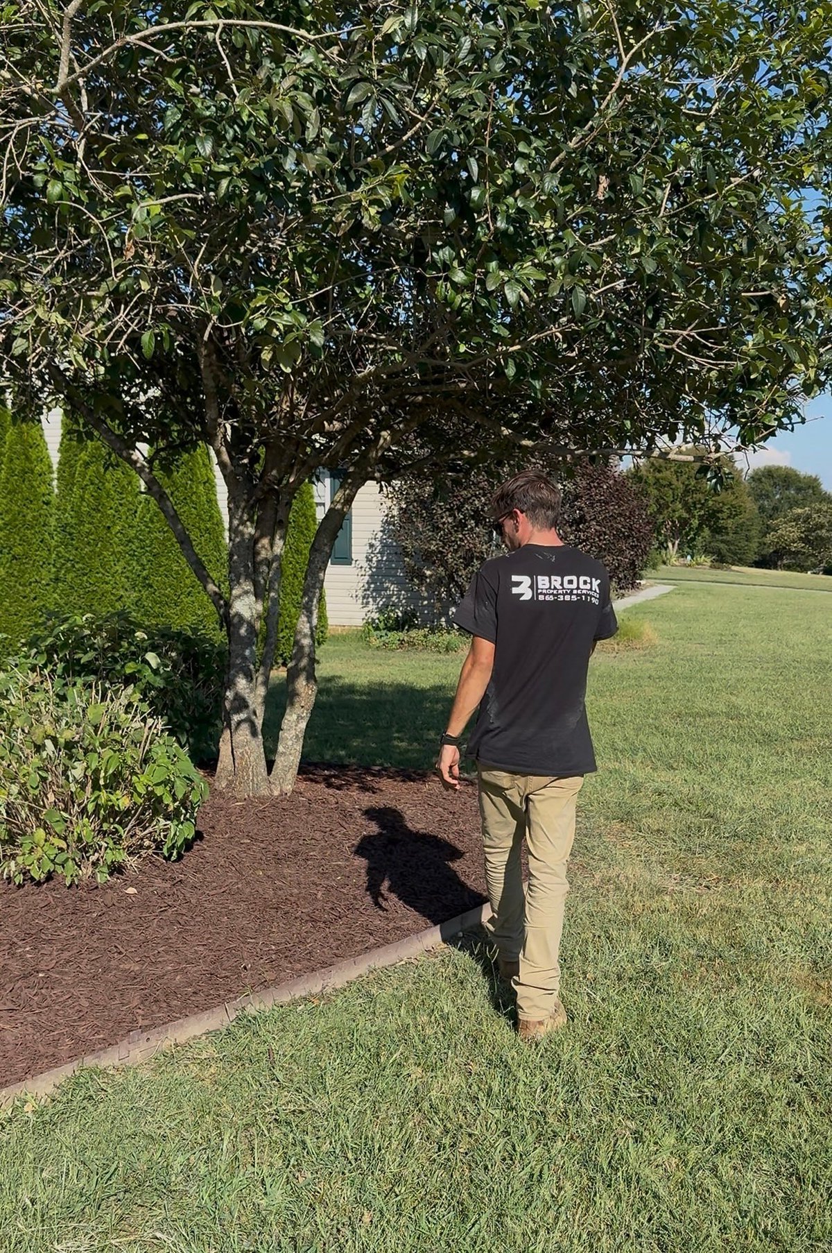 Brock Property Services crew member on a freshly maintained lawn beside a mulched tree bed